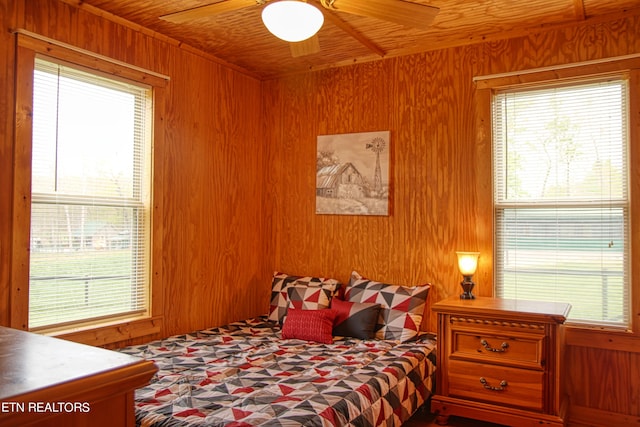 bedroom with wooden walls, ceiling fan, and multiple windows