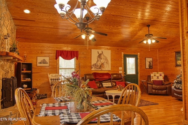 dining space featuring wood-type flooring, wood ceiling, ceiling fan with notable chandelier, and wooden walls