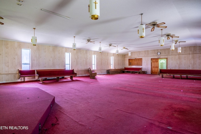 misc room featuring plenty of natural light, carpet, wooden walls, and ceiling fan