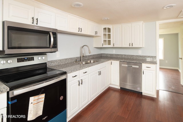 kitchen with light stone countertops, appliances with stainless steel finishes, white cabinetry, sink, and dark hardwood / wood-style flooring