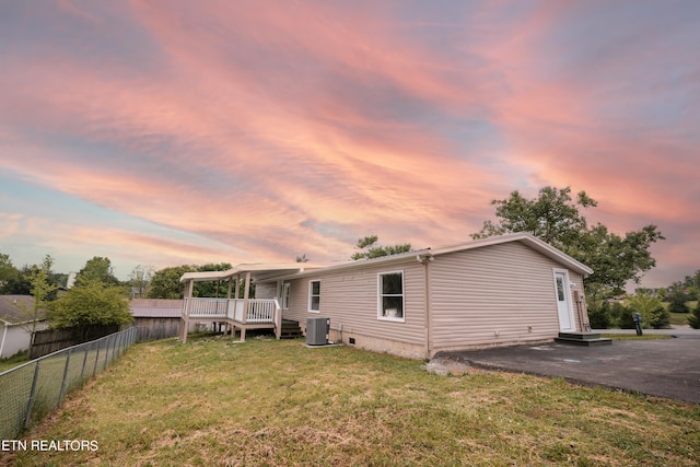 back house at dusk featuring a patio, a yard, a wooden deck, and central air condition unit