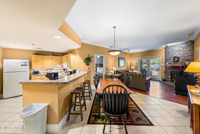 kitchen with hanging light fixtures, a breakfast bar area, white refrigerator, light tile floors, and ornamental molding