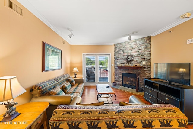 living room featuring a stone fireplace, hardwood / wood-style floors, ornamental molding, and track lighting