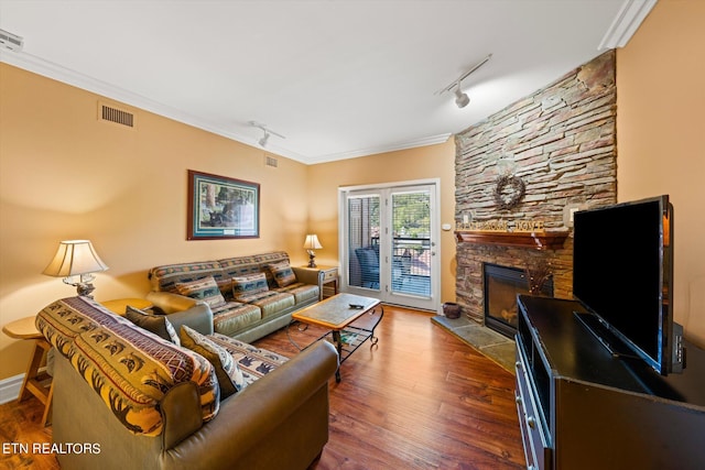 living room with ornamental molding, hardwood / wood-style flooring, track lighting, and a stone fireplace