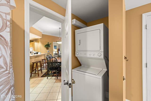 washroom with crown molding, stacked washer and dryer, and light tile floors