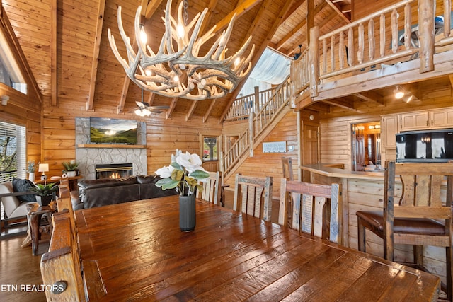 dining room with wood-type flooring, wood ceiling, high vaulted ceiling, and a stone fireplace