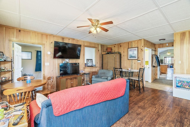 living room featuring a drop ceiling, wood walls, ceiling fan, and hardwood / wood-style flooring