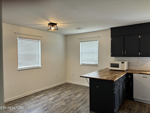 kitchen with dark hardwood / wood-style floors, white appliances, backsplash, and kitchen peninsula