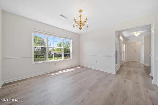 spare room featuring a notable chandelier and light hardwood / wood-style floors