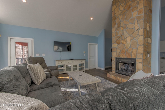 living room featuring vaulted ceiling, hardwood / wood-style flooring, and a stone fireplace