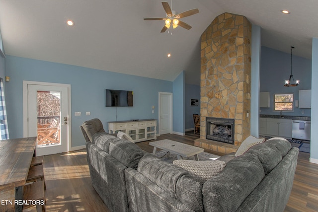 living room featuring high vaulted ceiling, a stone fireplace, ceiling fan with notable chandelier, dark hardwood / wood-style floors, and sink