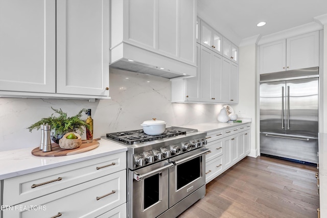 kitchen with crown molding, light hardwood / wood-style floors, premium appliances, white cabinetry, and backsplash