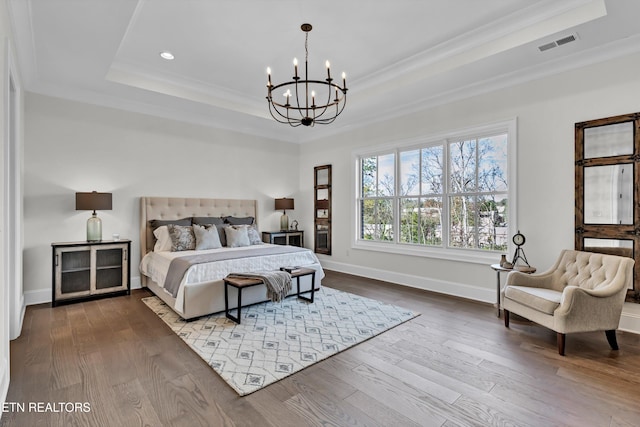 bedroom with hardwood / wood-style flooring, a tray ceiling, ornamental molding, and a notable chandelier