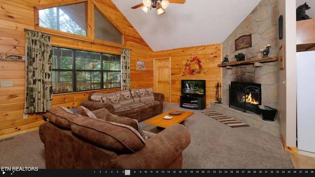 living room featuring ceiling fan, a stone fireplace, high vaulted ceiling, carpet flooring, and wooden walls