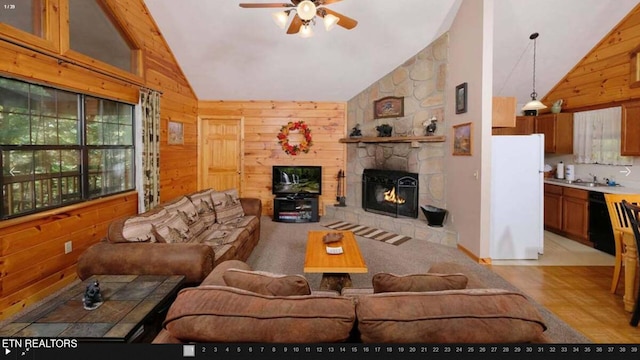 carpeted living room with wooden walls, a stone fireplace, high vaulted ceiling, and ceiling fan