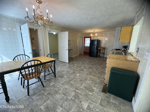 kitchen featuring a textured ceiling, decorative light fixtures, black fridge, and sink