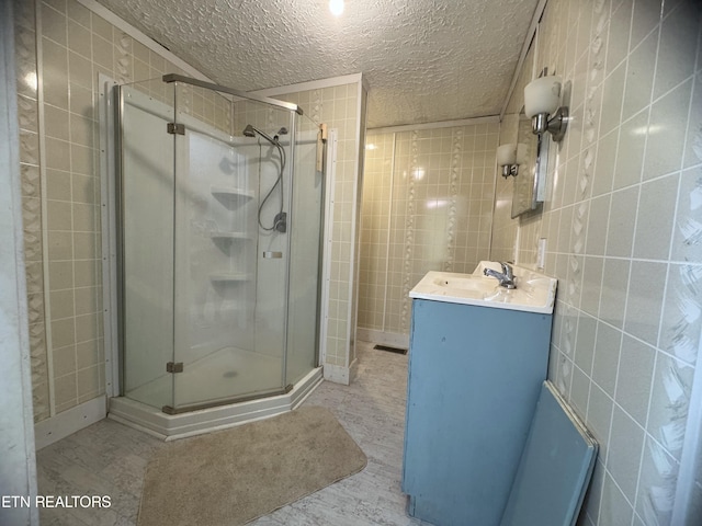 bathroom with walk in shower, vanity, tile walls, and a textured ceiling