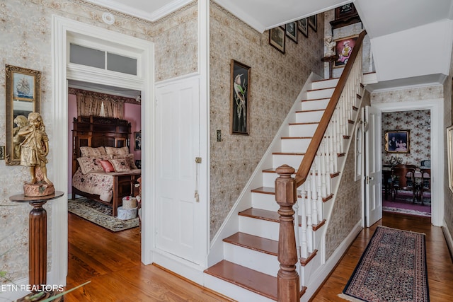 stairs with ornamental molding and hardwood / wood-style floors