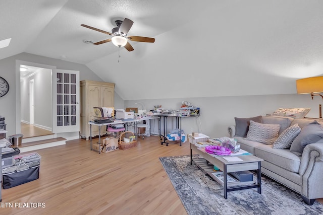 living room with lofted ceiling with skylight, ceiling fan, a textured ceiling, and light wood-type flooring