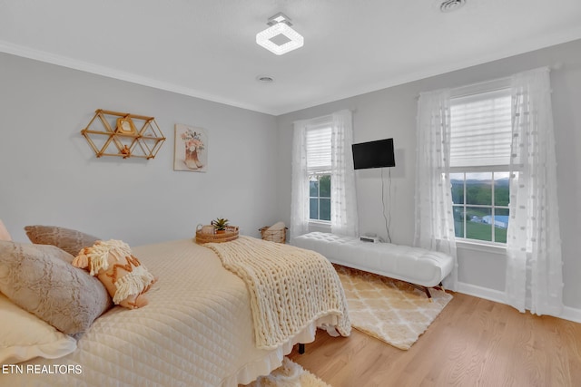 bedroom featuring ornamental molding, light hardwood / wood-style flooring, and multiple windows