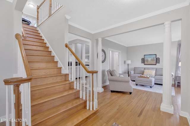 stairway with light hardwood / wood-style floors, crown molding, and ornate columns