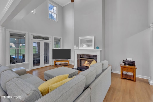 living room with french doors, a towering ceiling, light hardwood / wood-style floors, and a tile fireplace