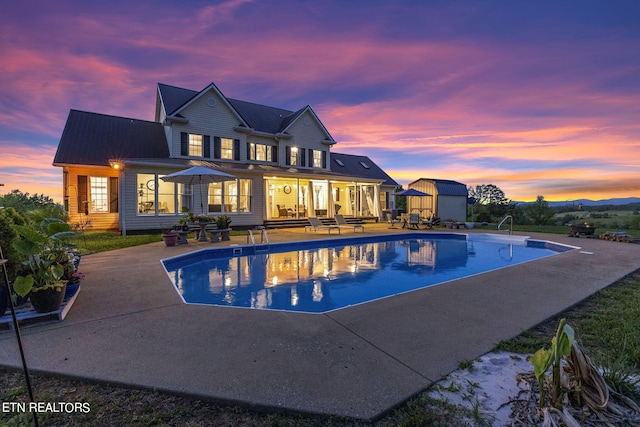 pool at dusk featuring a patio and an outdoor structure