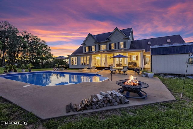 pool at dusk featuring an outdoor fire pit and a patio