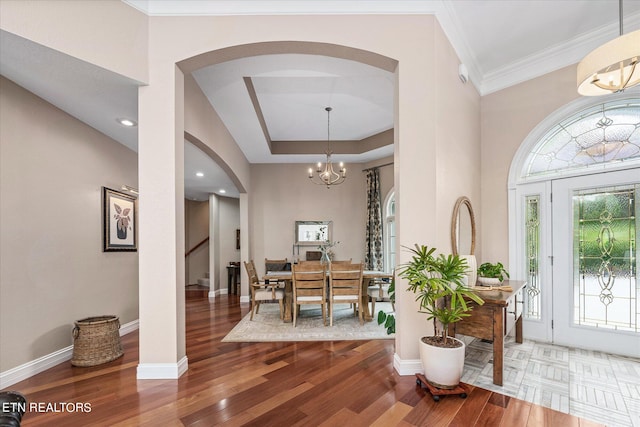 entryway with a raised ceiling, a notable chandelier, crown molding, and hardwood / wood-style floors