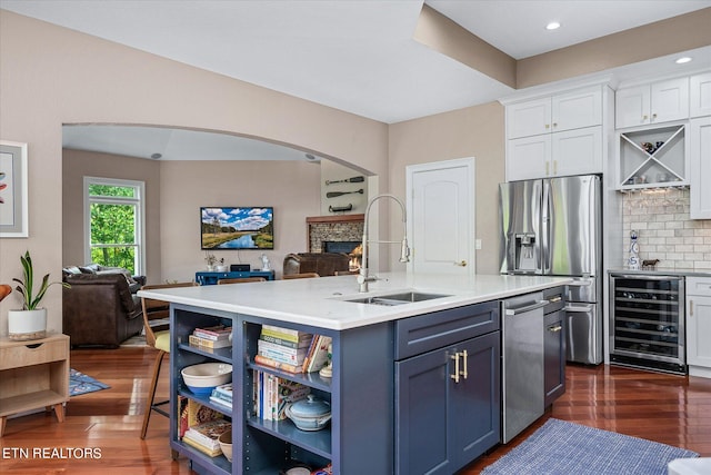 kitchen featuring appliances with stainless steel finishes, a kitchen island with sink, wine cooler, white cabinets, and sink