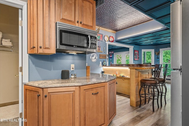 kitchen featuring light stone countertops, appliances with stainless steel finishes, light hardwood / wood-style floors, ornamental molding, and a breakfast bar