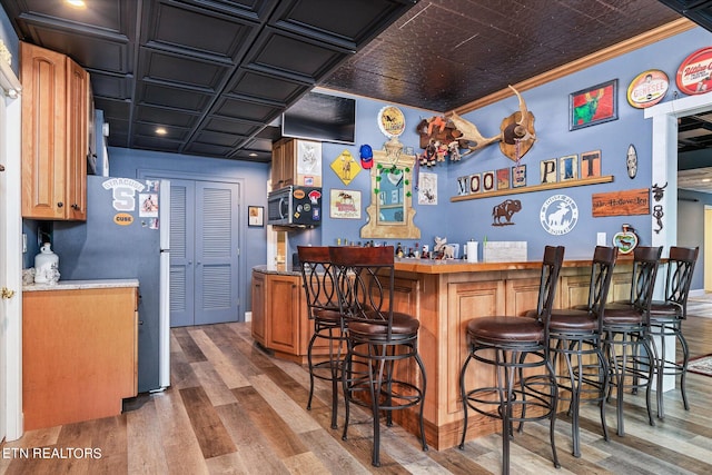 bar featuring dark wood-type flooring, ornamental molding, stainless steel appliances, and coffered ceiling