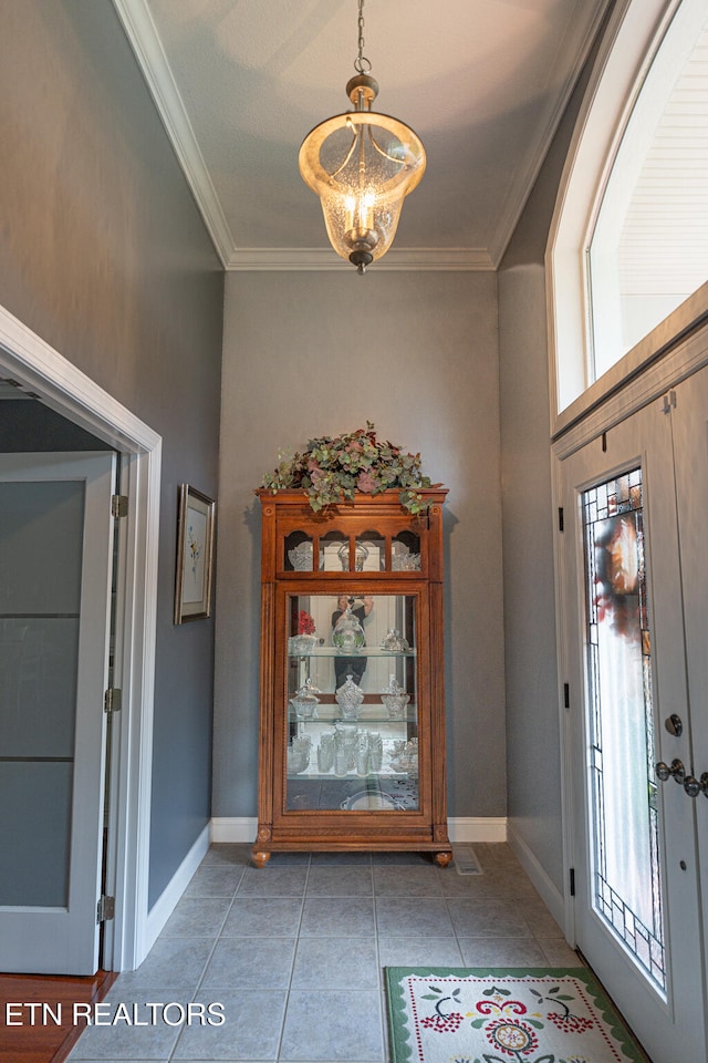 tiled entryway with crown molding and an inviting chandelier