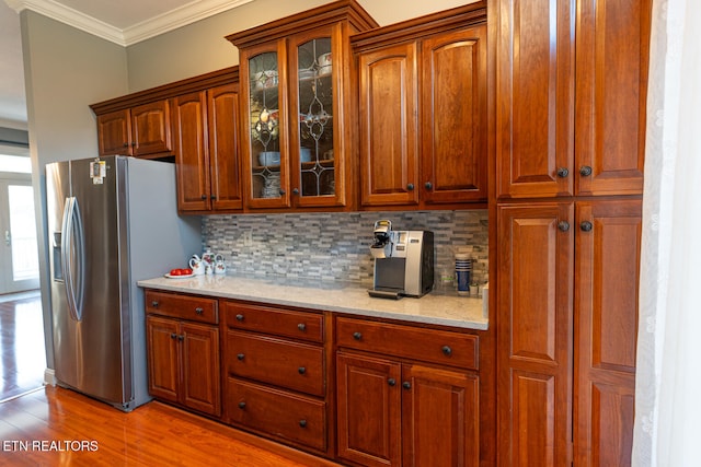 kitchen with crown molding, light wood-type flooring, backsplash, stainless steel fridge, and light stone counters