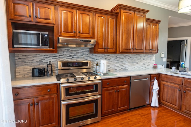 kitchen featuring hardwood / wood-style floors, tasteful backsplash, appliances with stainless steel finishes, crown molding, and sink