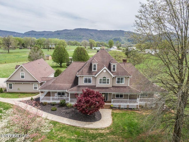 view of front of home with a mountain view, covered porch, and a front yard