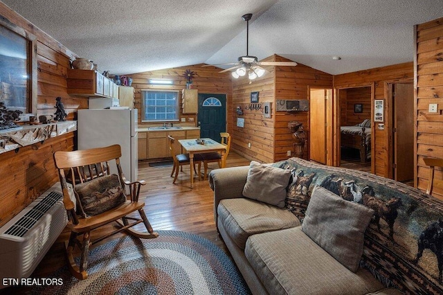 living room featuring lofted ceiling, wooden walls, sink, light hardwood / wood-style floors, and ceiling fan