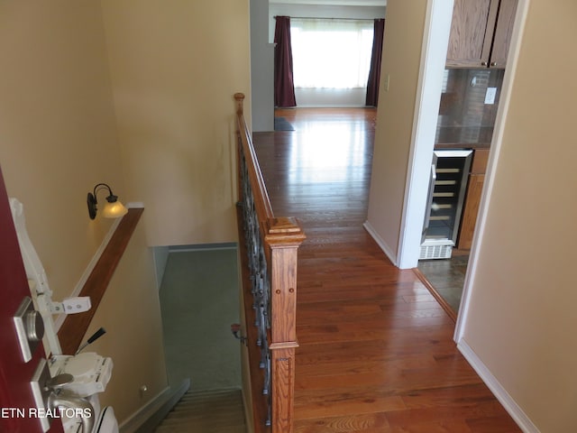 hall featuring beverage cooler, baseboards, wood finished floors, and an upstairs landing