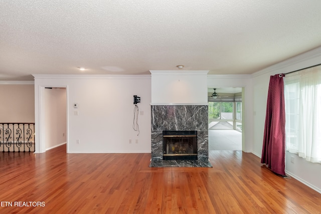 unfurnished living room with a textured ceiling, wood finished floors, a high end fireplace, baseboards, and crown molding