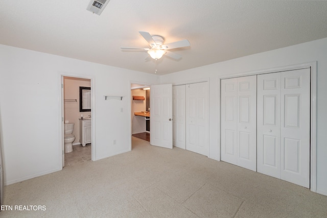 unfurnished bedroom featuring carpet, two closets, visible vents, a ceiling fan, and ensuite bath