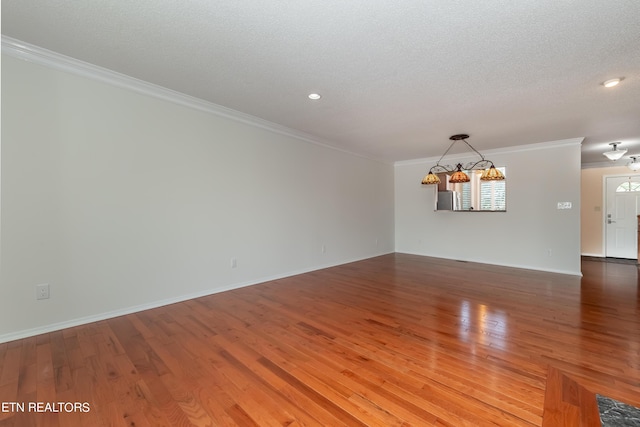 unfurnished room with a textured ceiling, ornamental molding, wood finished floors, and a chandelier