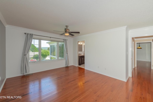 spare room featuring ceiling fan, wood finished floors, visible vents, baseboards, and crown molding