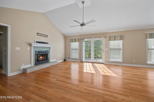 unfurnished living room featuring light hardwood / wood-style flooring, high vaulted ceiling, ceiling fan, and a tiled fireplace