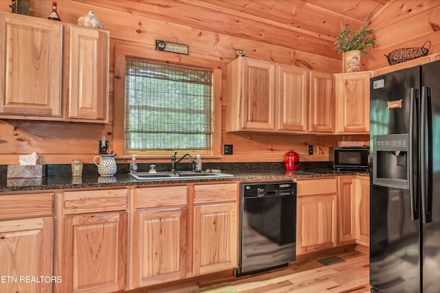 kitchen with black appliances, dark stone counters, wooden walls, sink, and light wood-type flooring