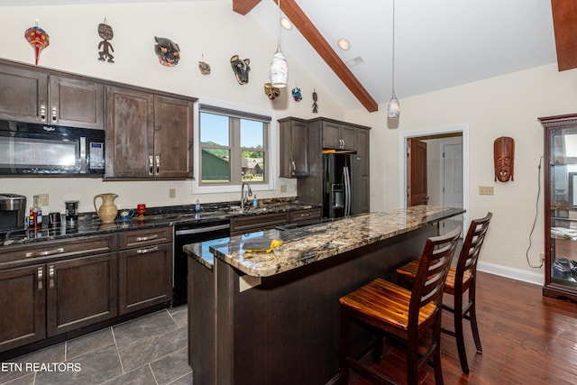 kitchen with decorative light fixtures, beamed ceiling, black appliances, dark stone countertops, and a center island