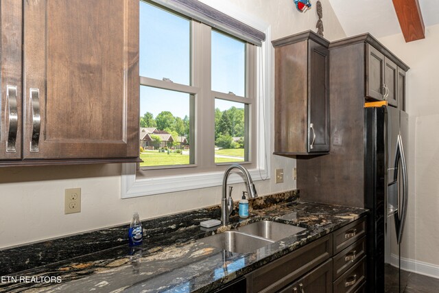 kitchen with stainless steel fridge with ice dispenser, sink, dark stone countertops, and dark brown cabinets