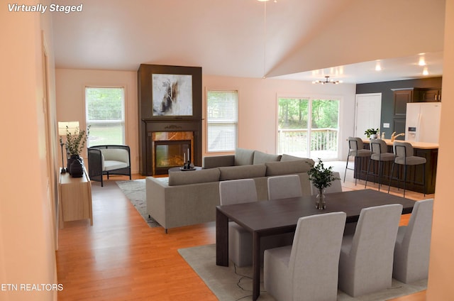 dining space featuring a fireplace, an inviting chandelier, light hardwood / wood-style floors, and vaulted ceiling