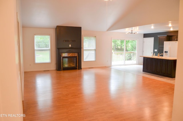 unfurnished living room featuring sink, light hardwood / wood-style flooring, a notable chandelier, a premium fireplace, and lofted ceiling