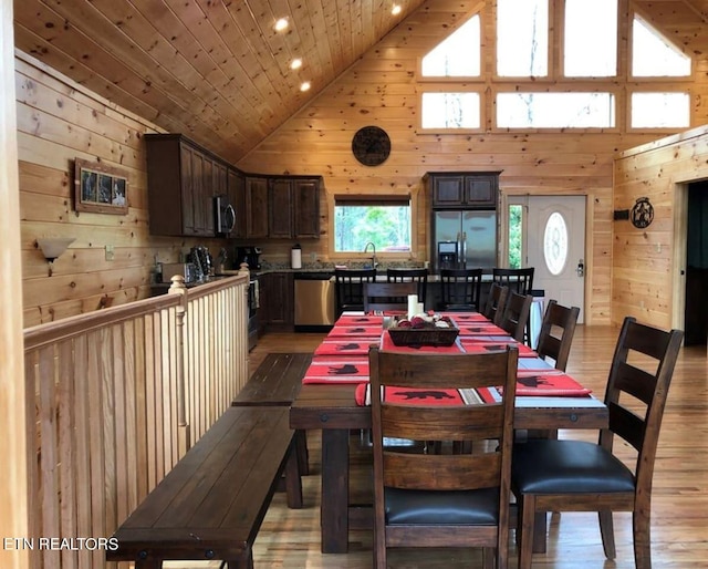 dining room featuring wood ceiling, wood walls, light hardwood / wood-style floors, and high vaulted ceiling