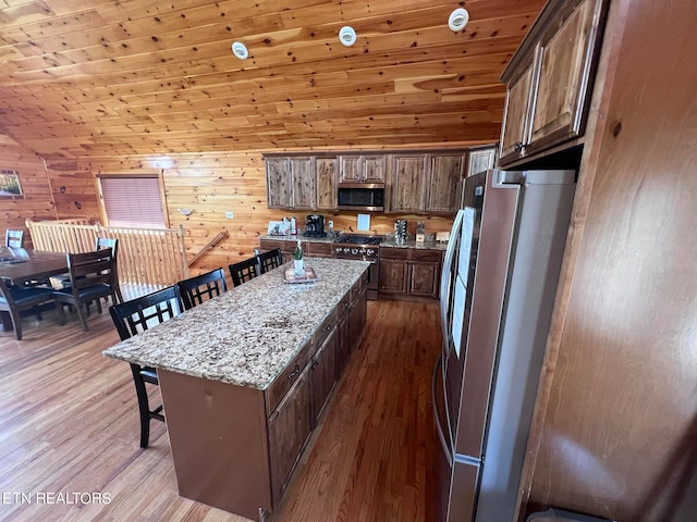 kitchen featuring wood walls, wood-type flooring, wooden ceiling, stainless steel appliances, and light stone counters